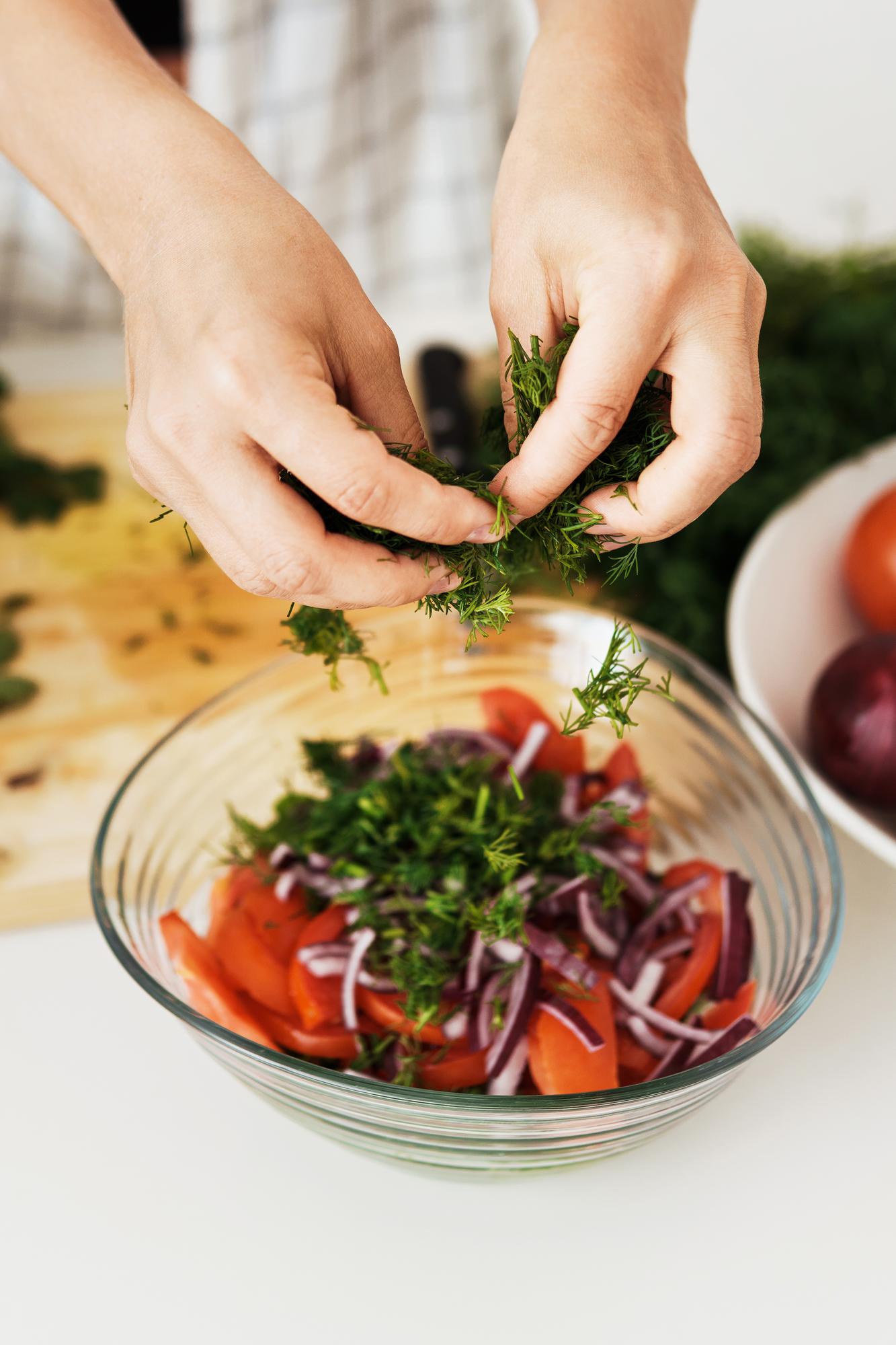 Hands garnishing salad with herbs